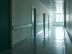 orredor vazio de hospital, com portas fechadas em sequência e luz natural entrando por uma janela ao fundo